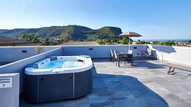 Une terrasse sur le toit avec un jacuzzi, des sièges extérieurs et une vue sur la mer et les collines.