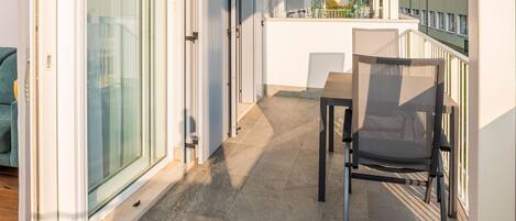 A balcony with a table and chairs, a sliding glass door, and a view of buildings and greenery.