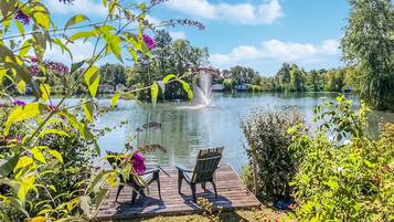 Une jetée en bois avec deux chaises donnant sur un lac, entourée d’une végétation luxuriante et agrémentée d’une fontaine.