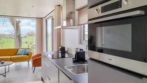 Ett modernt kök med en stor ugn, en kaffebryggare och utsikt över ett grönskande landskap genom stora fönster.