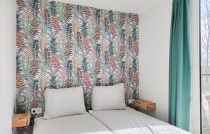 A bedroom with a patterned headboard, two pillows, a wooden bedside table, and a view of the outdoors through a window. - Lovely home in Oosterwolde with WiFi (Oosterwolde)