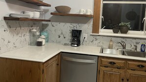 A kitchen with wooden cabinets, a dishwasher, a coffee maker, and a window with a view. - The Adolphus - 4 Bedrooms, 2 Baths. Sleeps 8 comfortably!  (Oak Harbor)