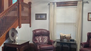 A room with a wooden staircase, a chandelier, a large window with blinds, and two leather chairs. - The Adolphus - 4 Bedrooms, 2 Baths. Sleeps 8 comfortably!  (Oak Harbor)