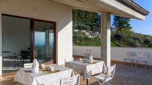 Un patio al aire libre con dos mesas preparadas para comer, sillas blancas y vistas a una colina.