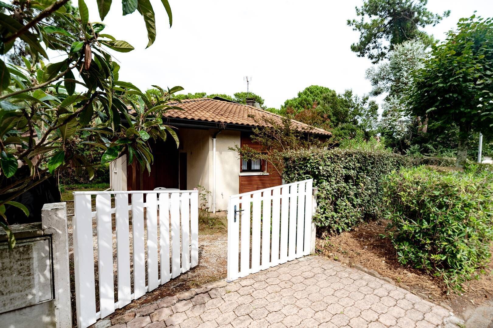 A small house with a tiled roof, a white picket fence, and a paved entrance.