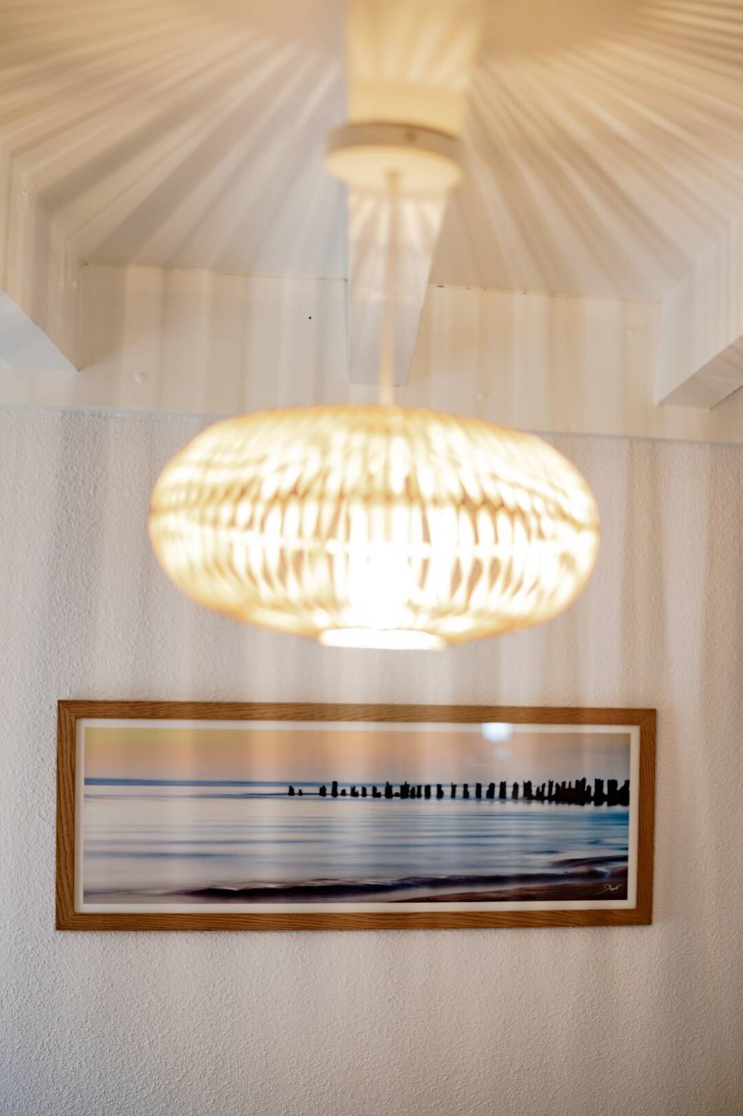 A ceiling with a textured design and a hanging pendant light. Below, there is a framed picture on the wall.