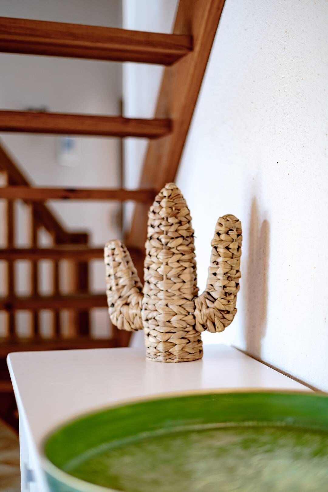 Une sculpture de cactus tissée, placée sur une surface blanche près d’un escalier.