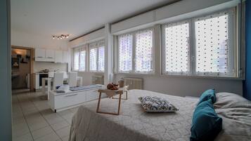 Une chambre moderne avec un lit, une petite table sur laquelle se trouve une bouilloire, et une vue sur la ville grâce à de grandes fenêtres.