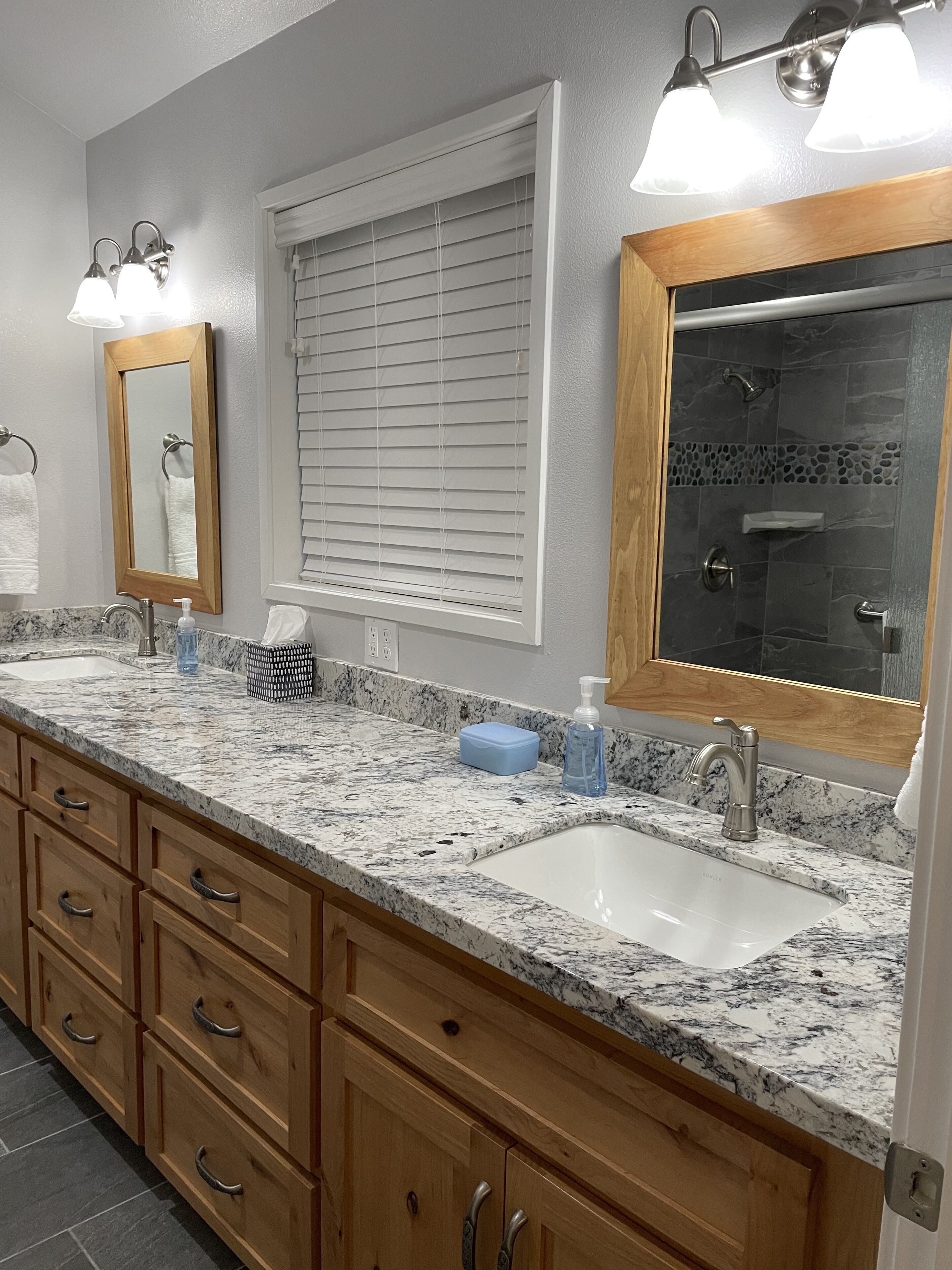 A bathroom with a double sink vanity, wooden cabinets, a large mirror, and a shower area.