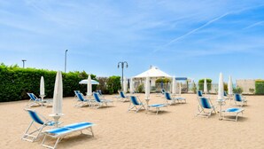 Een strandgedeelte met meerdere ligbedden en parasols, een kiosk en een heldere lucht.