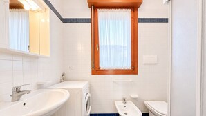 Een badkamer met een wastafel, wasmachine, bidet en toilet.