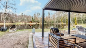 Eine überdachte Terrasse mit Sitzgelegenheiten, einem Teich und einer Hütte im Hintergrund.