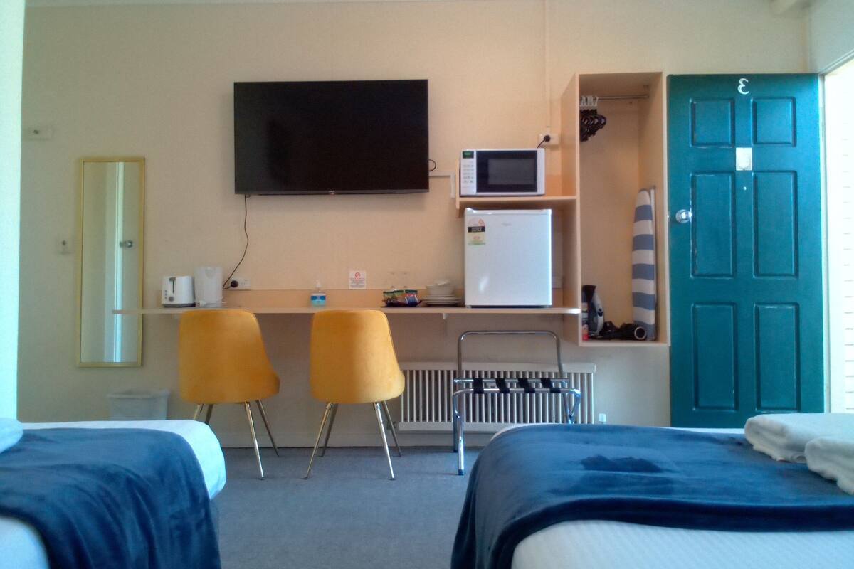 A hotel room with two beds, a desk with a TV, a microwave, and a refrigerator.