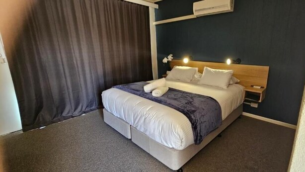 Habitación de hotel con cama, mesita de noche, aire acondicionado instalado en la pared y cortina.