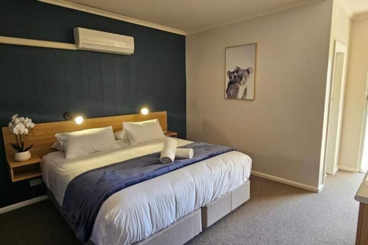 A bedroom with a bed, bedside table, and a wall-mounted air conditioner.