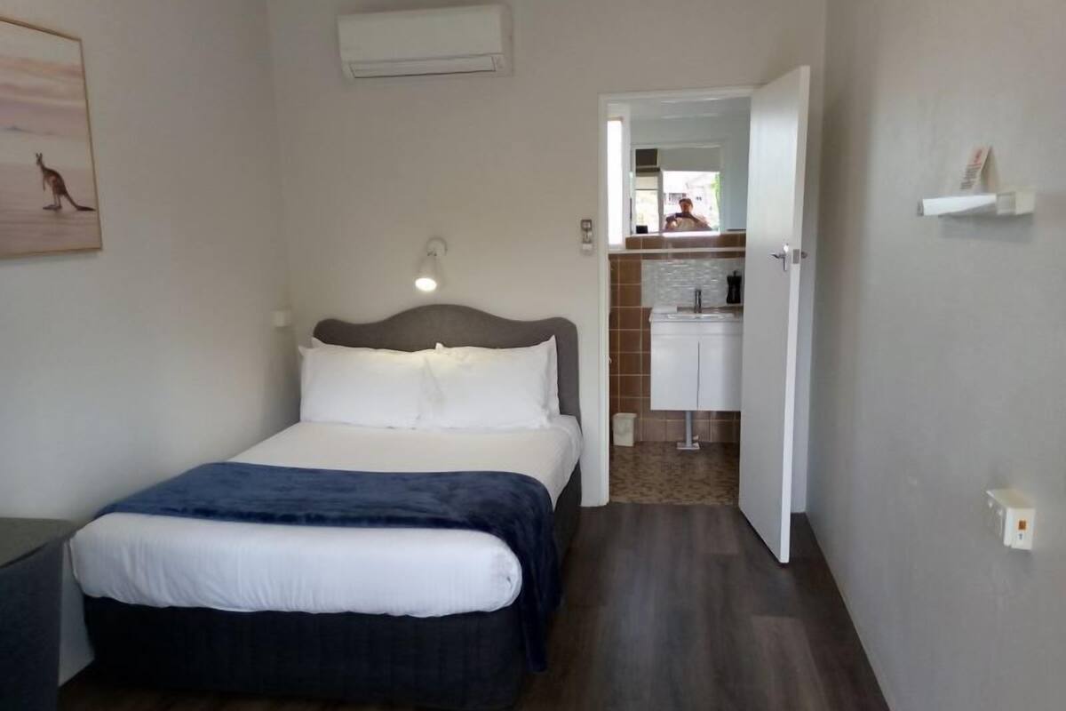 A bedroom with a bed, bedside table, and a wall-mounted air conditioner.