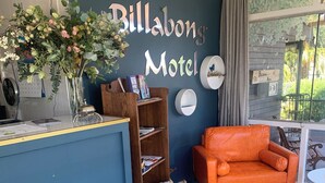 Una habitación con mostrador azul, estantería de madera, sofá naranja y una pared con el letrero 'Billabong Motel'.