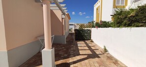 A narrow alleyway with a tiled floor, white walls, and a yellow building in the background.