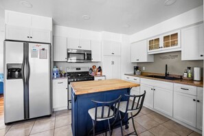 Una cocina moderna con armarios blancos, electrodomésticos de acero inoxidable, una isla central con sillas y un microondas integrado.