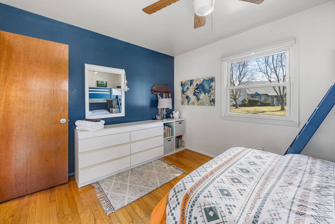 A bedroom with a bed, a dresser, a mirror, a window, and a door.