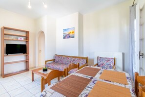 Una habitación con televisión, sofá, mesa, sillas y un cuadro en la pared.