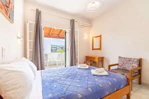 A bedroom with a bed, a chair, a small table, and a view through a door. - Apartment 'Olivea Apt 4' with Sea View, Wi-Fi and Air Conditioning (Corfu)
