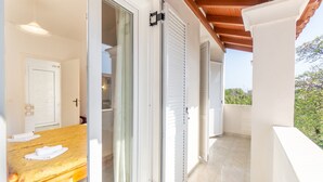 Une chambre avec un lit, un banc en bois, des portes-fenêtres coulissantes et un balcon avec vue.