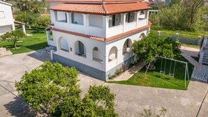 Un bâtiment à deux étages, doté d’un toit en tuiles, de fenêtres en arc de cercle et d’un petit jardin avec une balançoire.