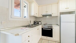 Une cuisine avec des armoires blanches, une cuisinière en acier inoxydable, un four encastré, un réfrigérateur blanc et une fenêtre avec vue.