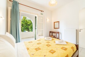 Quarto de hotel com cama, janela com cortinas, mesa de cabeceira, espelho e radiador.