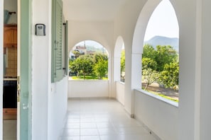 Corredor com tetos em arco, vista para vegetação e edifícios lá fora, e piso de azulejos.