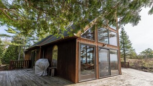 A wooden cabin with a deck, large sliding glass doors, and a covered grill area.