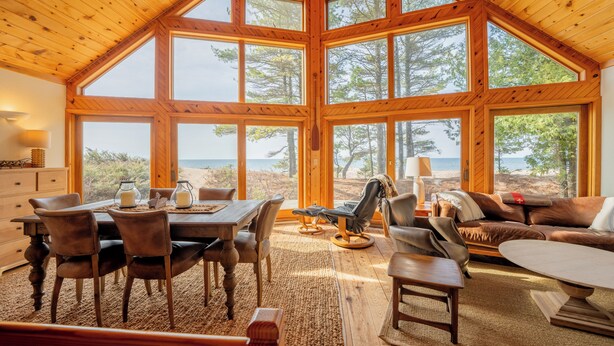 A spacious room with a high ceiling and large windows, a dining area with a table and chairs, and a seating area with a sofa and armchairs.