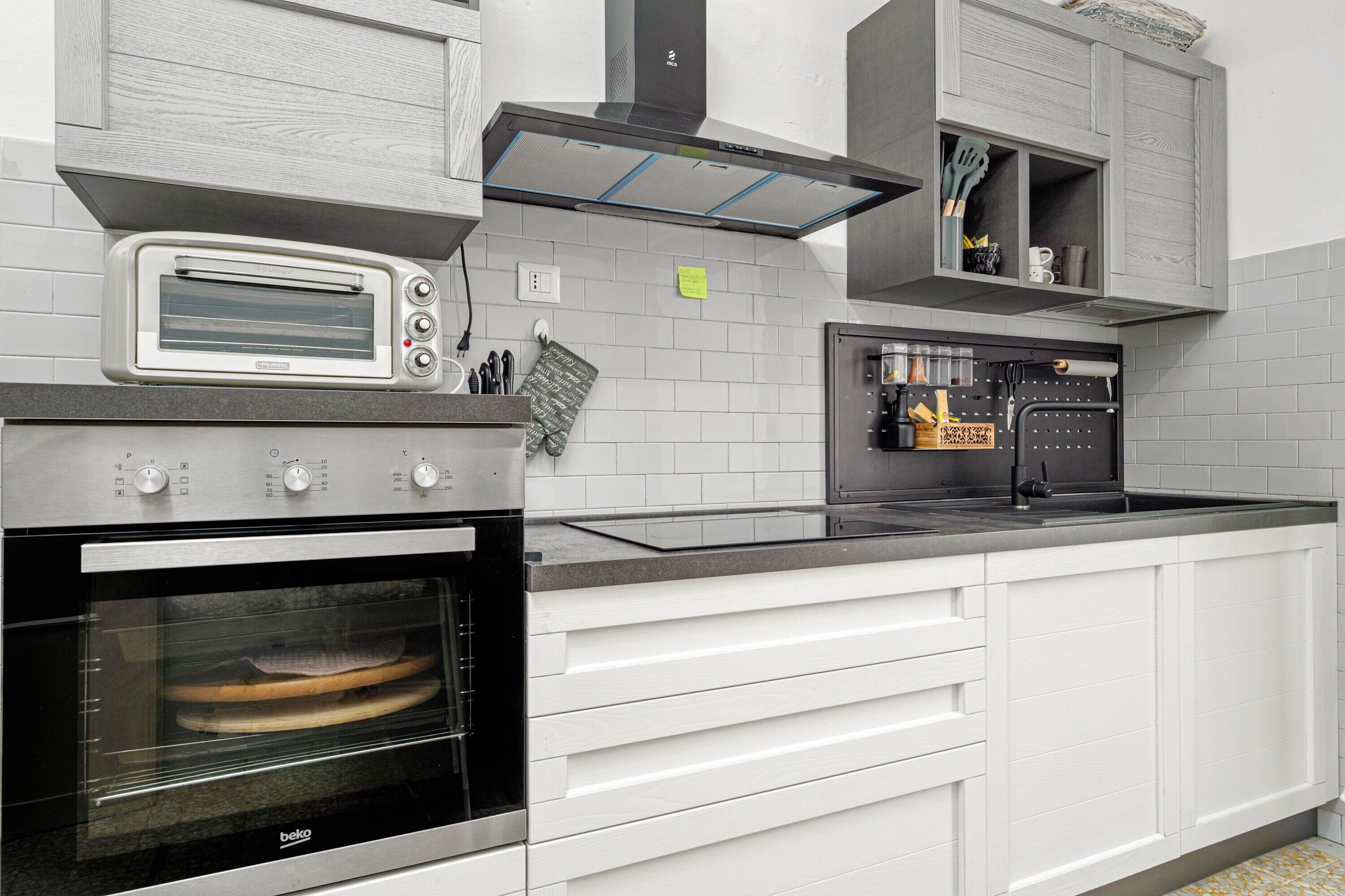 Una cucina con forno a incasso, forno nero, pensili bianchi e lavello in acciaio inossidabile.