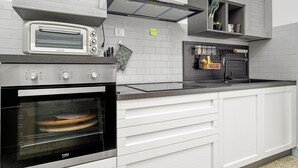 Une cuisine équipée d’un four à grille-pain encastré, d’un four noir, de meubles blancs et d’un évier en acier inoxydable.