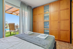 Ein Schlafzimmer mit einem Bett, einem Holzschrank und Blick auf einen Pool.