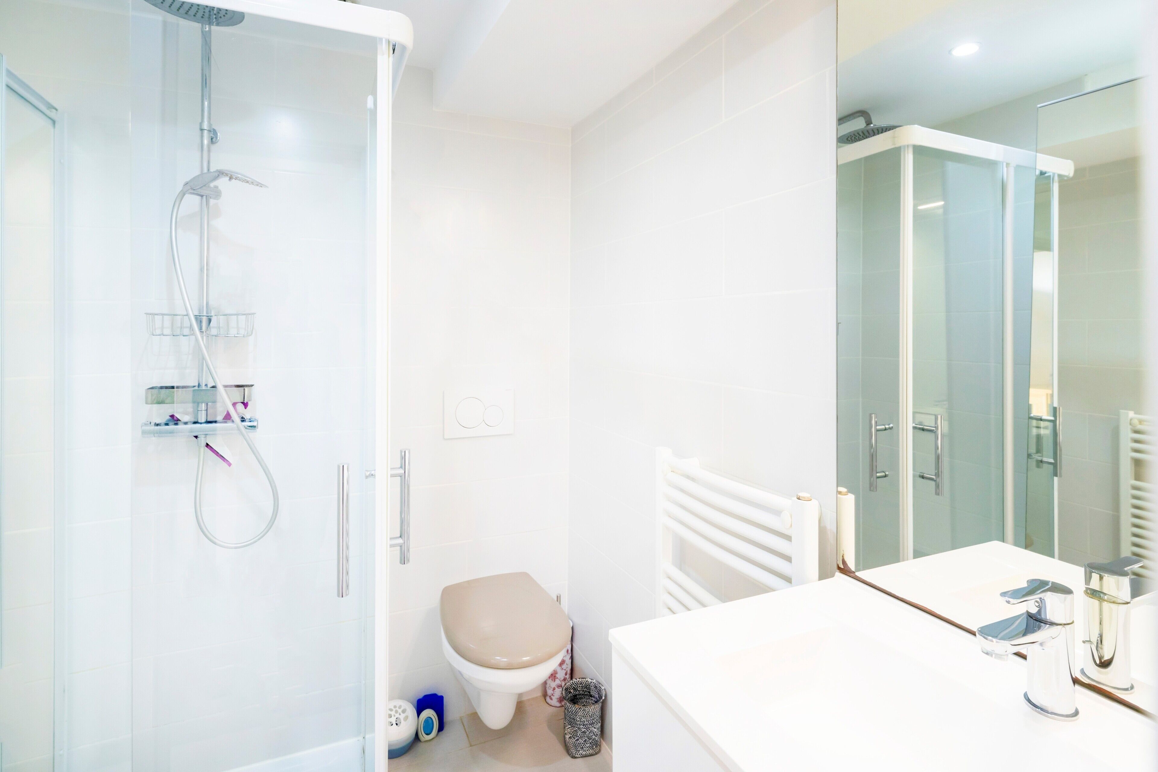 A modern bathroom with a glass shower enclosure, a toilet, a sink with a mirror, and a towel rack.