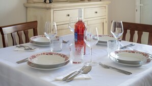Una mesa de comedor dispuesta con platos, vasos, cubiertos, una botella de vino y un cuenco decorativo al fondo.