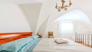 Un dormitorio con cama, mesita de noche, silla y ventana con cortinas.