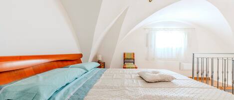 Un dormitorio con cama, mesita de noche, silla y ventana con cortinas.