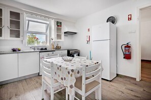 Una cucina con mobili bianchi, un tavolo da pranzo con tovaglia decorata e un frigorifero bianco.