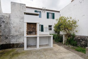 Un edificio bianco con persiane verdi, un piccolo balcone e un albero nel cortile.