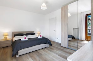 A modern bedroom with a bed, bedside lamps, a mirror, and a wooden floor.