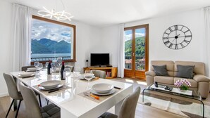 Een moderne woonkamer met een eetgedeelte, grote ramen met uitzicht op de bergen, een bank en een wandklok.
