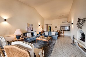Een woonkamer met een bank, salontafel, stoelen, een open haard en een eethoek met een tafel en stoelen.