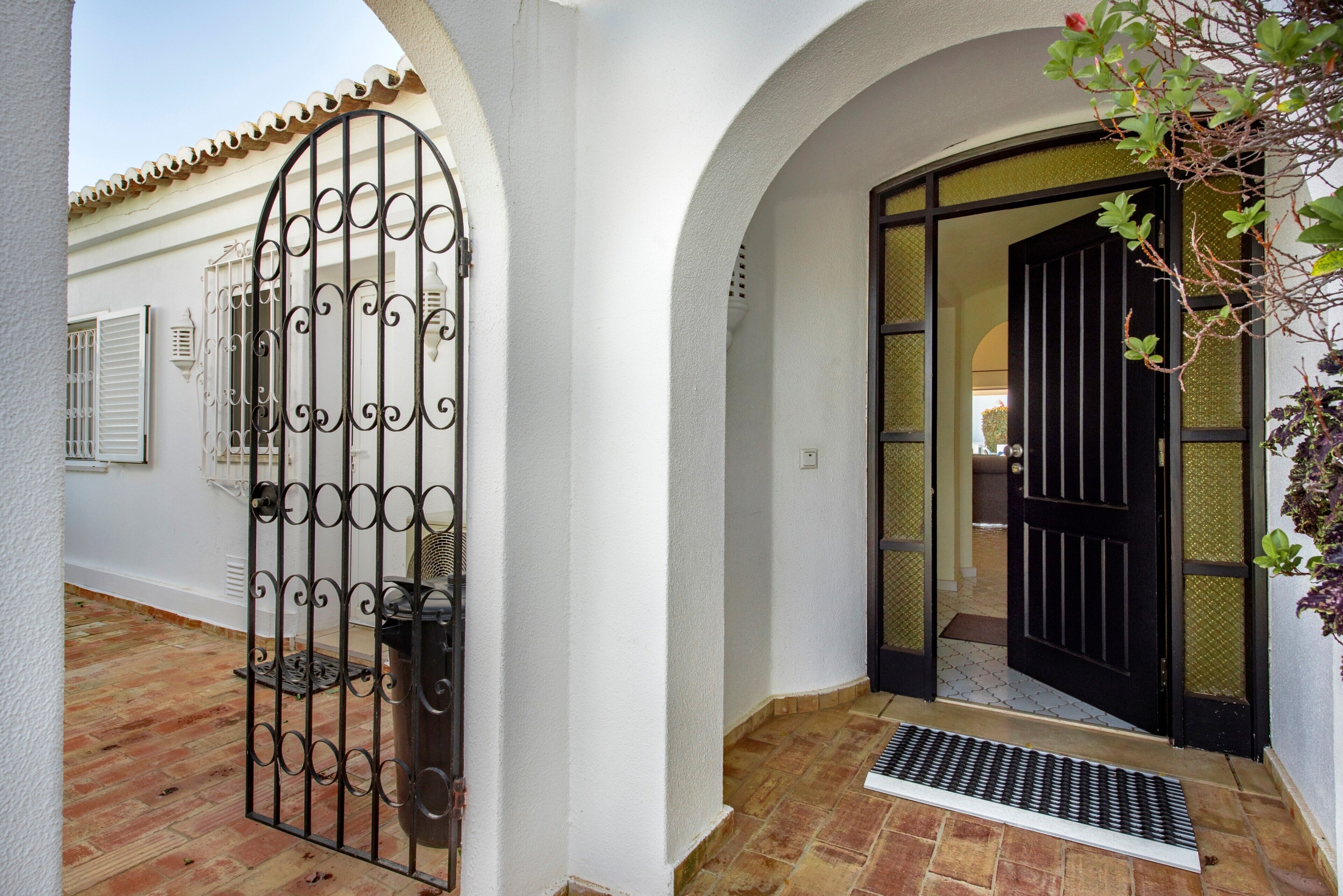 A white building with a black gate, a tiled entrance, and a small plant.