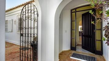 A white building with a black gate, a tiled entrance, and a small plant.