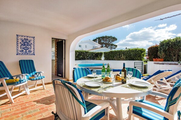 Een terras met een ronde tafel, stoelen en uitzicht op een huis en bomen.