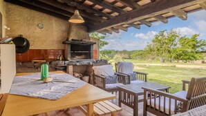 An outdoor patio with a stone fireplace, wooden furniture, and a view of the surrounding landscape.