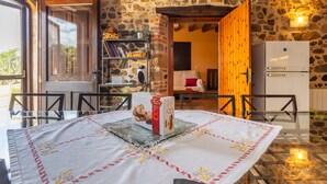A rustic stone interior with a dining table, chairs, a bookshelf, a refrigerator, and a wooden door.